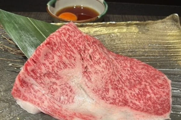 美しい霜降りが特徴の高級和牛肉が、笹の葉と共に盛り付けられています。奥には卵黄が入った小鉢があり、すき焼きやしゃぶしゃぶなどの料理に使われる前の準備段階のようです。