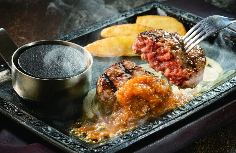 熱々の鉄板に盛り付けられたジューシーなハンバーグステーキの写真です。