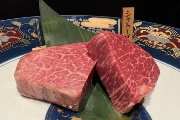 美しい霜降りの入った高級牛肉の塊が2切れ、飾り付けられた皿に盛られています。