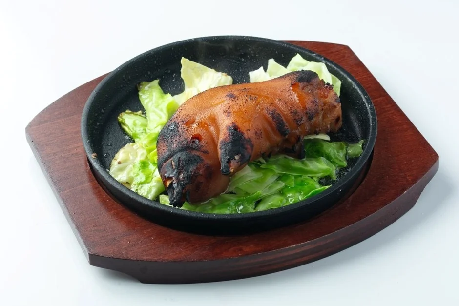 熱々の鉄板に盛り付けられた、香ばしく焼き上げられた豚足とキャベツの料理。食欲をそそる焦げ目が特徴的な一品です。