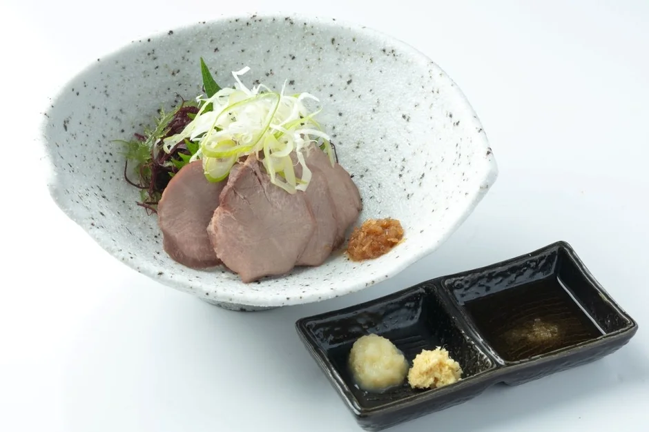 白い背景に置かれた和食の一品で、薄切り肉（牛タンまたは豚肉）が盛り付けられた陶器の器が中央にあります。肉の上には白髪ネギと青菜が添えられ、薬味としておろし生姜、おろし大根、醤油が別の小皿に用意されています。