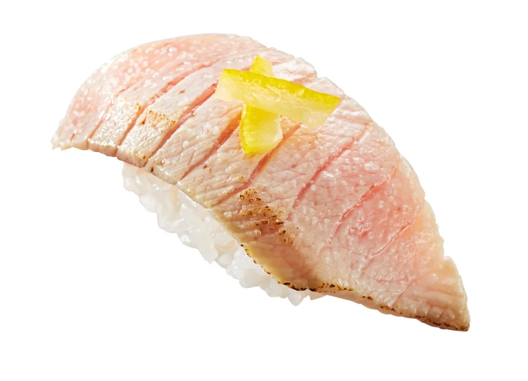 軽く炙られたとろけるようなマグロの握り寿司が一つ写っています。ご飯の上にピンク色のネタが乗り、その上には黄色い薬味が添えられています