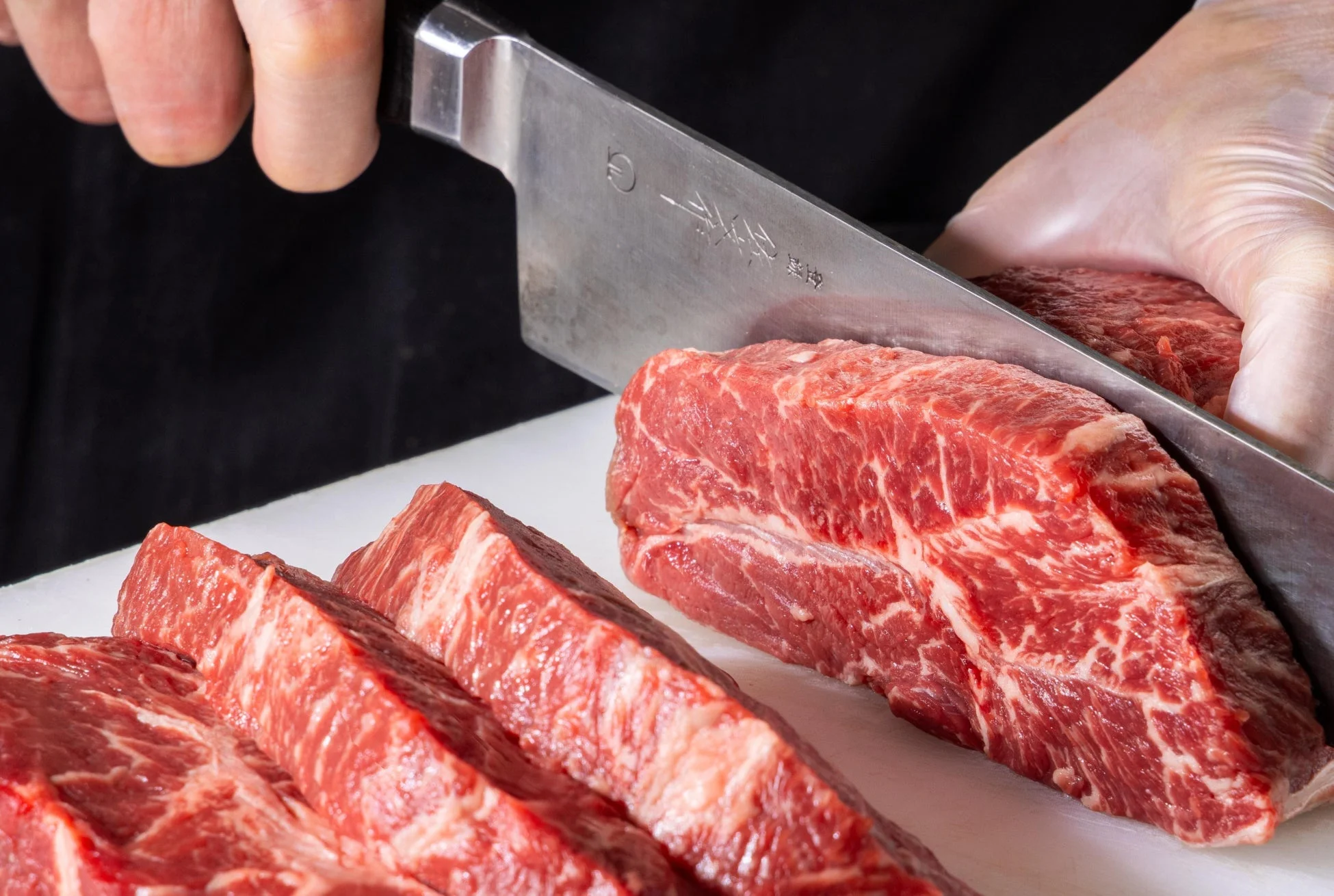 白いまな板の上で、新鮮な塊肉の牛肉を包丁でスライスしている様子。