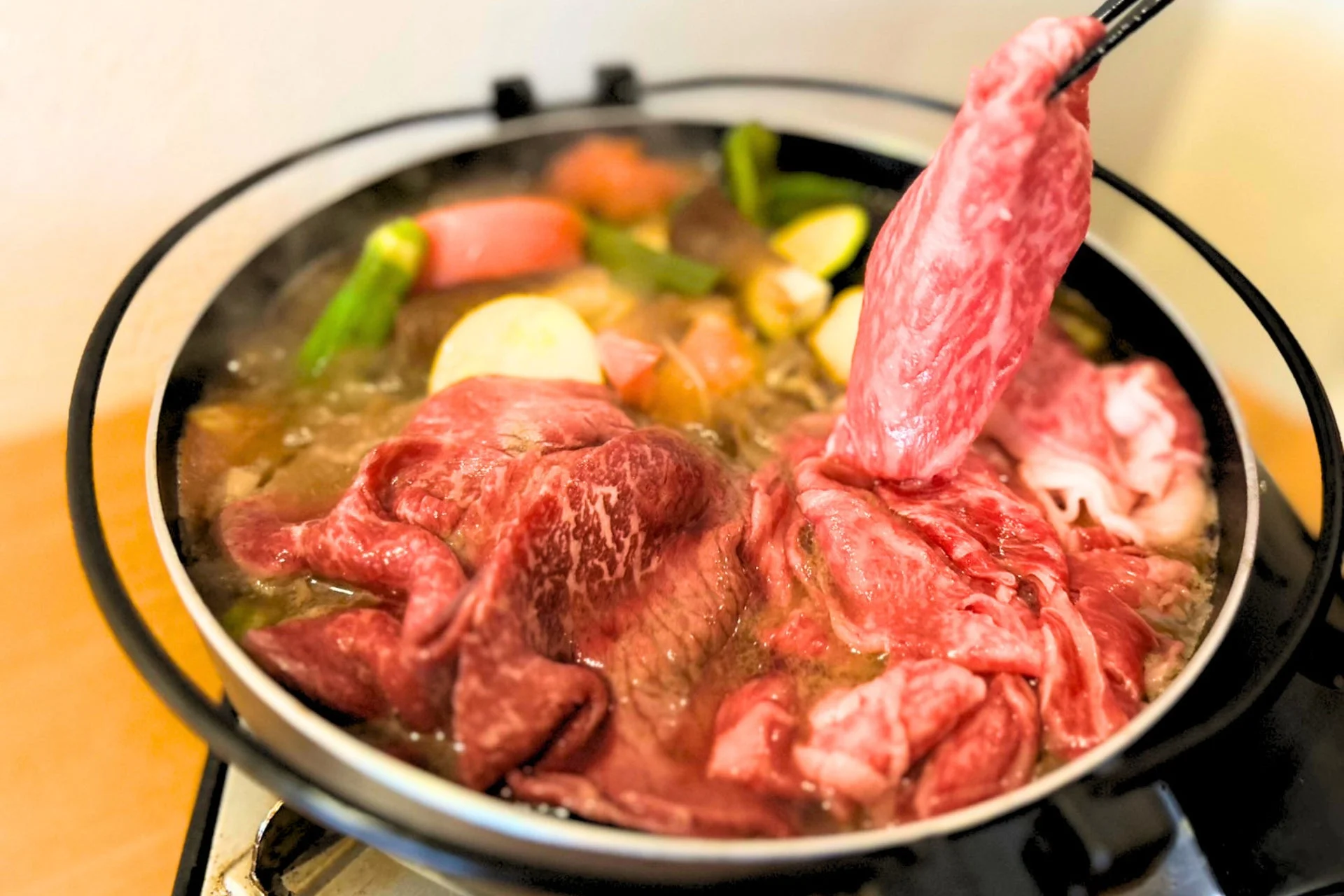 湯気の立つ鍋の中で煮込まれる薄切りの牛肉と様々な野菜