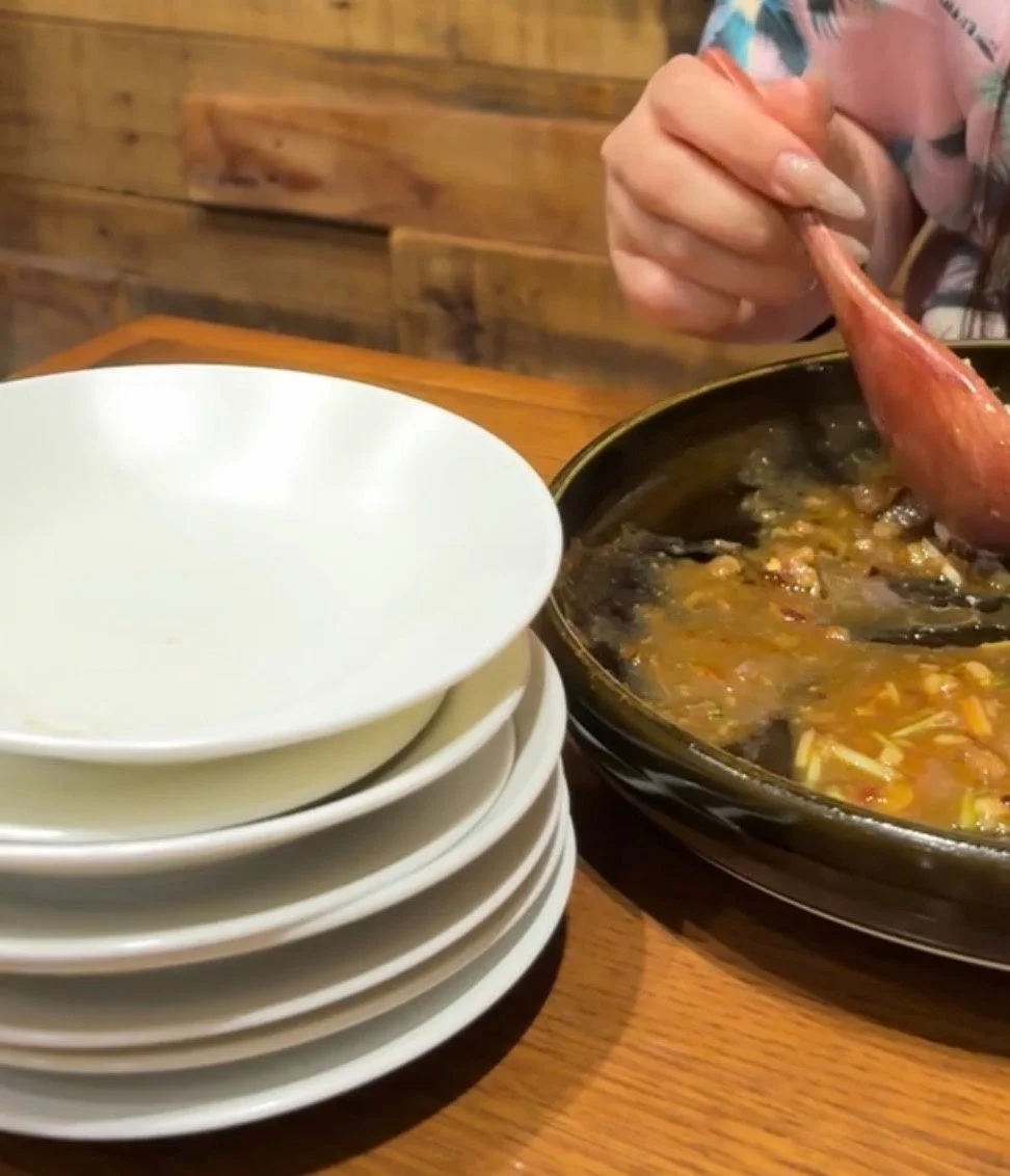 食卓で、一人の人物が大きなボウルに入った料理を木製のスプーンで取り分けている様子です。