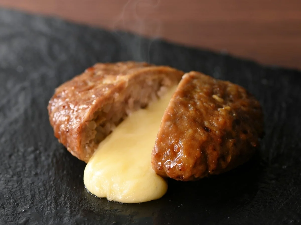 熱々のチーズインハンバーグが半分にカットされ、中からとろりと溶けたチーズがあふれ出ている様子