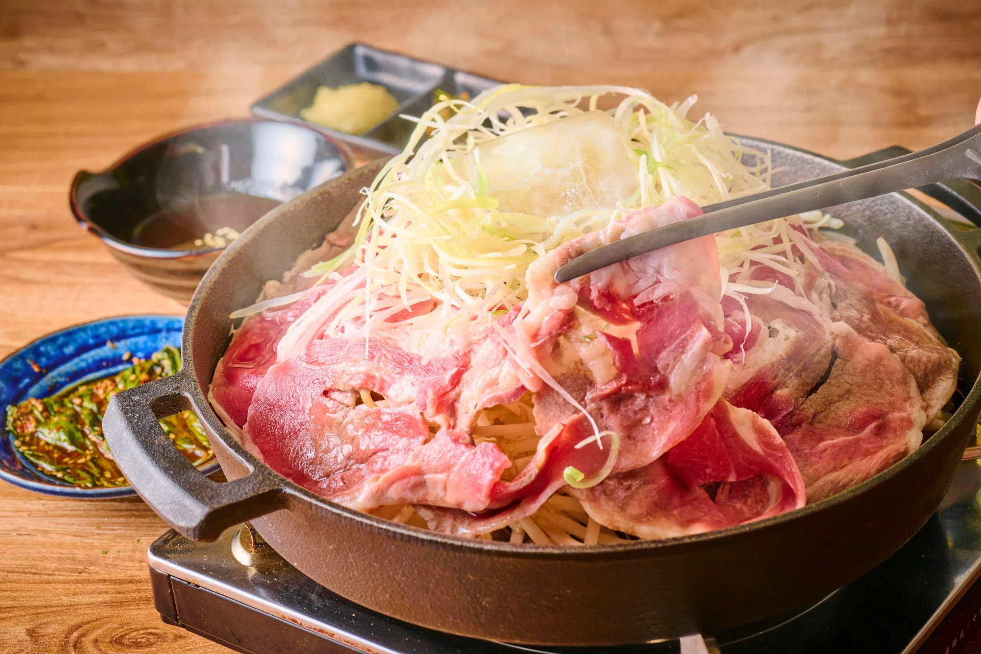 薄切りの肉と大量の千切り野菜が鉄鍋に盛られ、調理されている様子