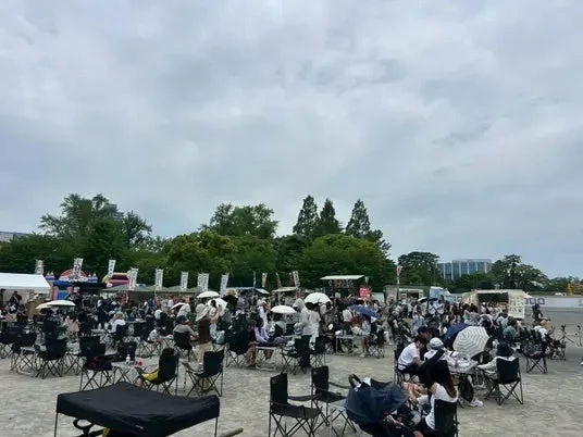 曇り空の下、屋外の広場で多くの人々が集まり飲食を楽しむイベント風景