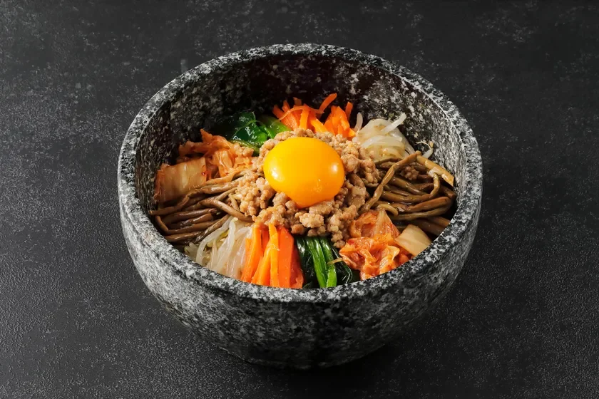 石の器に入ったビビンバで、色とりどりのナムル、ひき肉、キムチ、そして中央に鮮やかな卵黄が盛り付けられています