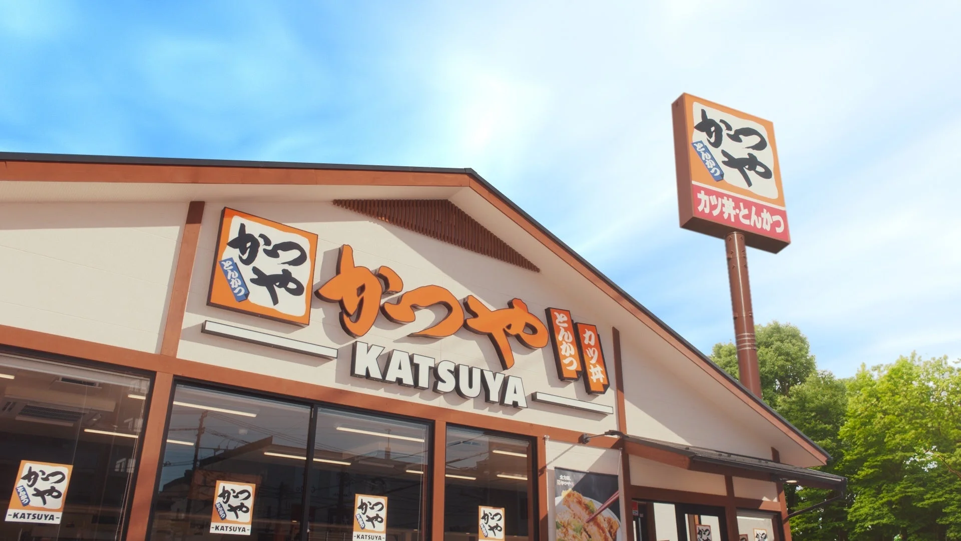 青空の下に建つ「かつや」店舗の外観写真。大きな看板と建物に「かつや」「Katsuya」「カツ丼・とんかつ」の文字が見える。