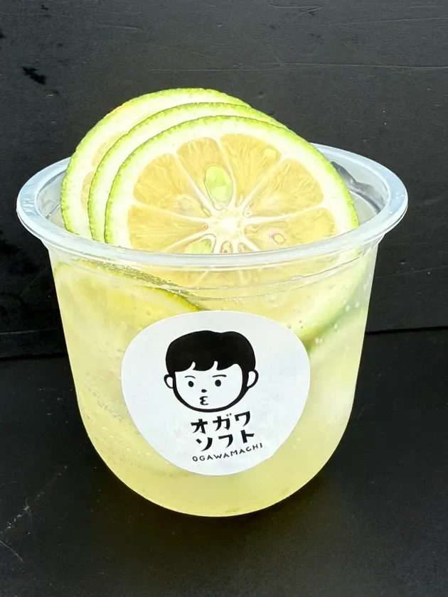 透明なプラスチックカップに入った、柑橘系のスライスが数枚トッピングされた冷たいドリンクです。カップには「オガワソフト OGAWAMACHI」と書かれたロゴシールが貼られています。