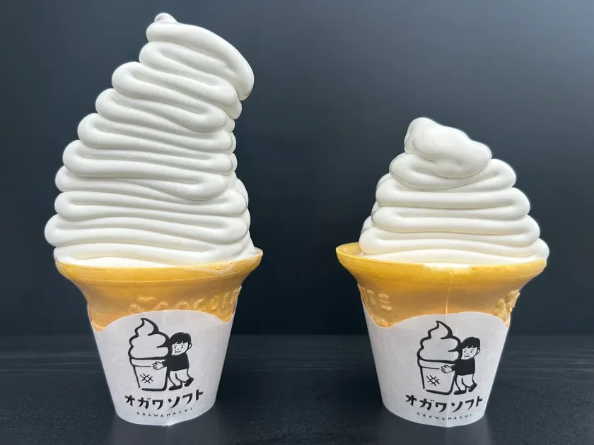 黒い背景をバックに、ワッフルコーンに入った大小2つの白いソフトクリームが並んでいます。コーンには「オガワソフト」と書かれたロゴがあり、大きい方は特にボリューム感があります。