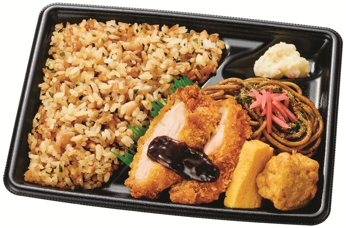 黒い容器に入ったお弁当で、炊き込みご飯、チキンカツ、焼きそば、ポテトサラダ、卵焼き、揚げ物など様々な和風のおかずが盛り合わせられています