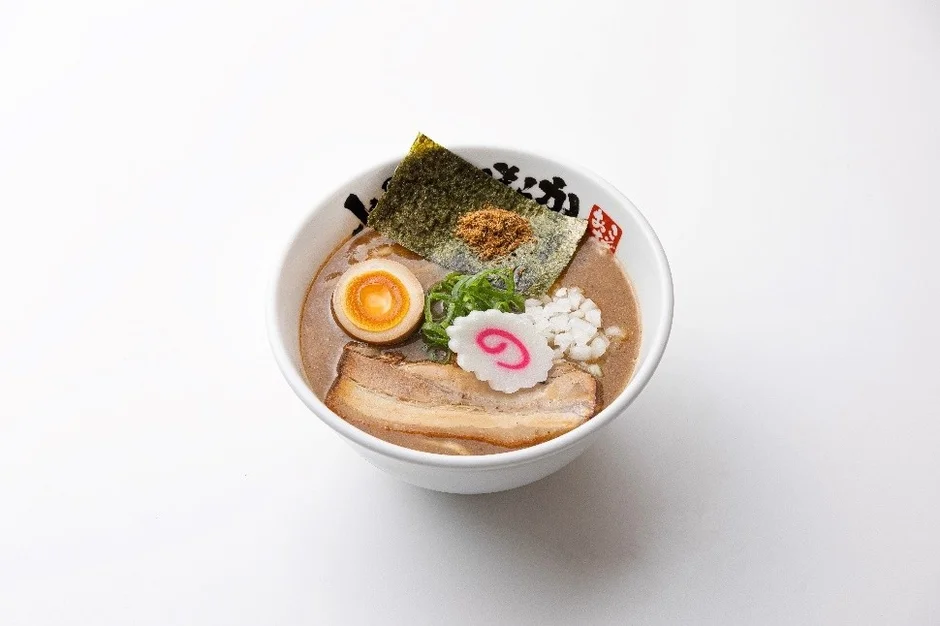 白い背景に置かれた、濃厚な豚骨スープが特徴の家系ラーメン。チャーシュー、半熟卵、海苔、なると、刻みネギが美しく盛り付けられており、食欲をそそる一杯です。