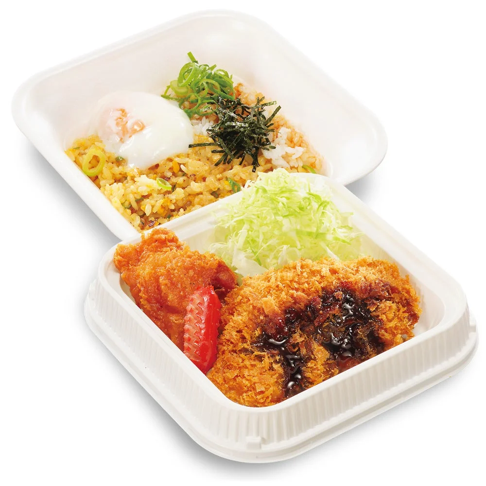 白いテイクアウト容器に入った日本の弁当。上段には温泉卵とネギがのったチャーハン、下段にはソースのかかった揚げ物、唐揚げ、千切りキャベツ、トマトが盛り付けられています。